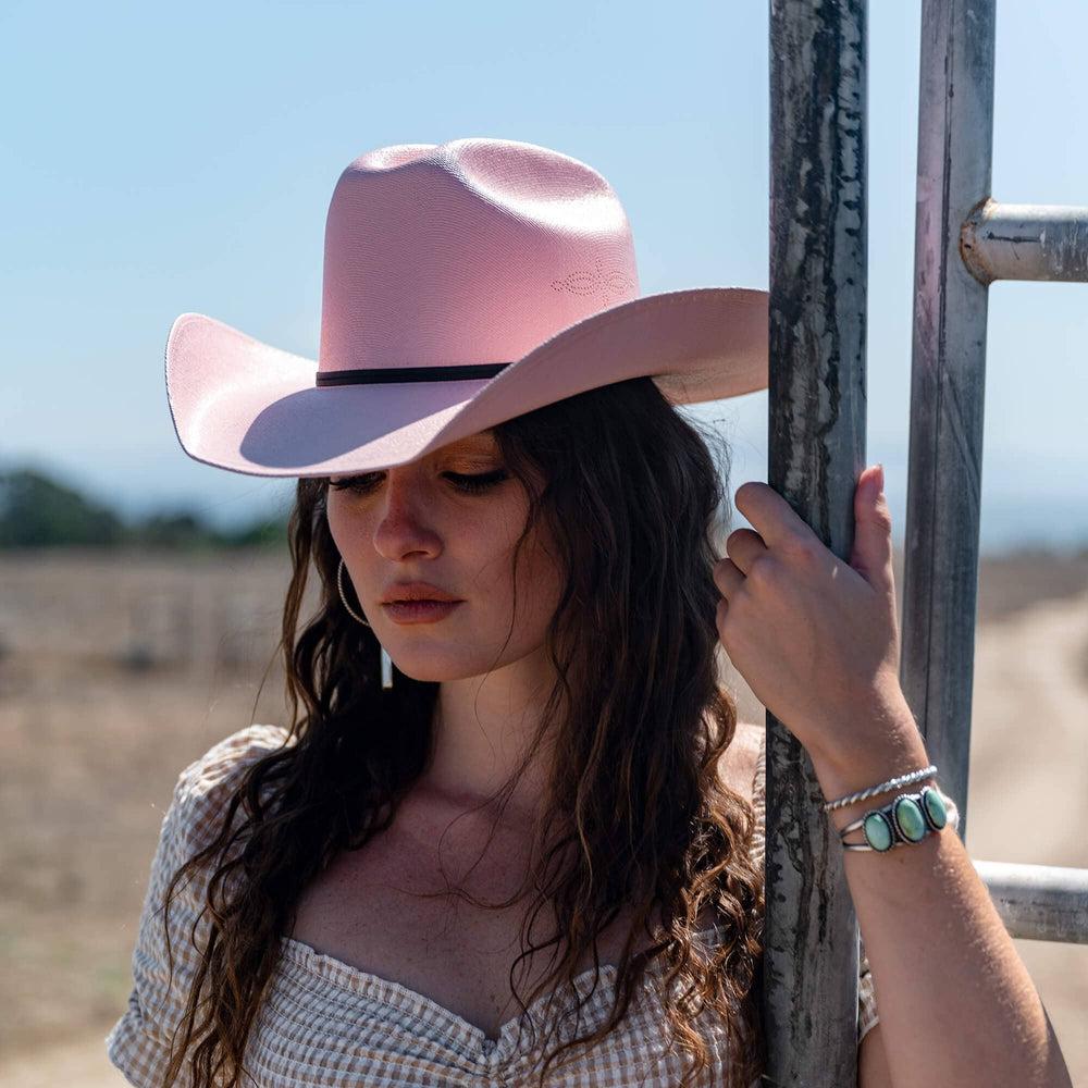 A woman holding a steel fence and wearing Pink Straw Cowboy Hat 