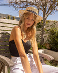 A woman sitting outdoors wearing Saunter Natural Straw Sun Hat 