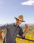 A man standing on a mountain view wearing Cubana Straw Sun Hat 