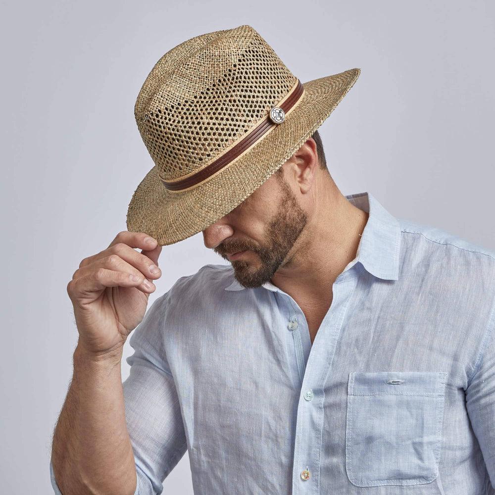 A man wearing Seagrass Cubana Straw Sun Hat while holding it on right hand