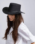 A woman facing side view and looking downwards wearing a black hat